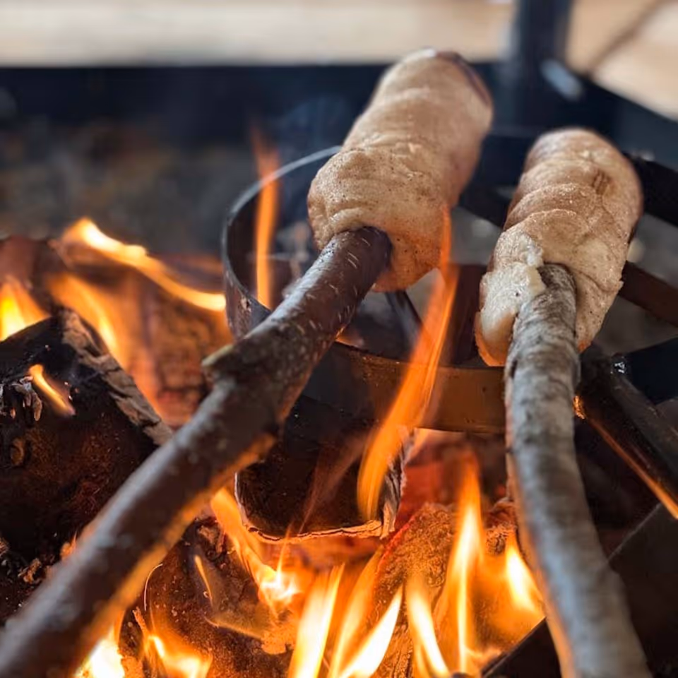 Two pieces of dough wrapped around sticks being roasted over an open flame fire.