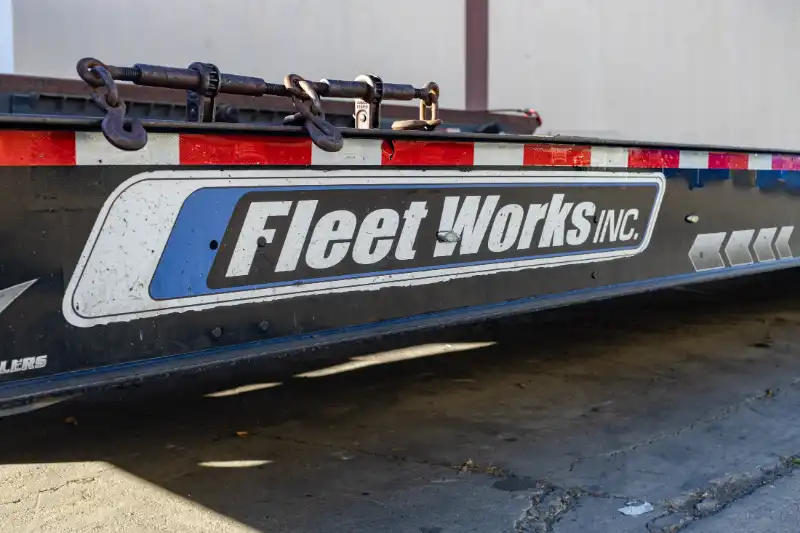 Peterbilt tractor and lowboy flatbed trailer parked outside shop for fleet maintenance; Fleet Works logo on door.