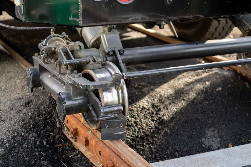 Hi-rail gear system mounted to a utility vehicle axle, aligned on rusted railroad track for rail access.