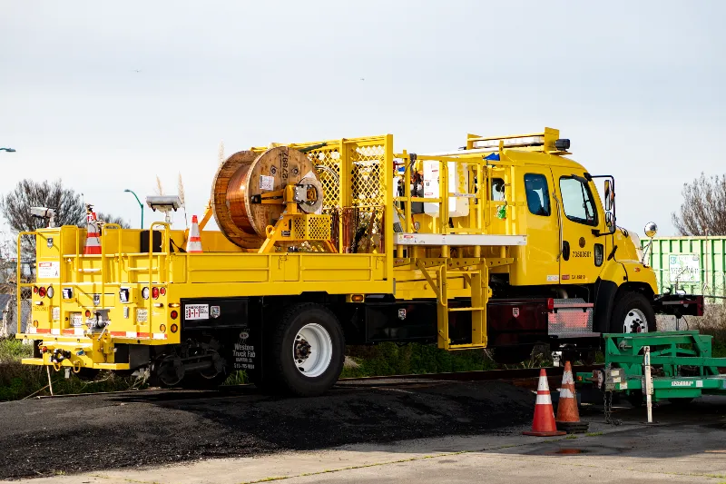 Utility service truck with mounted cable reel and safety cones parked on a paved work zone.