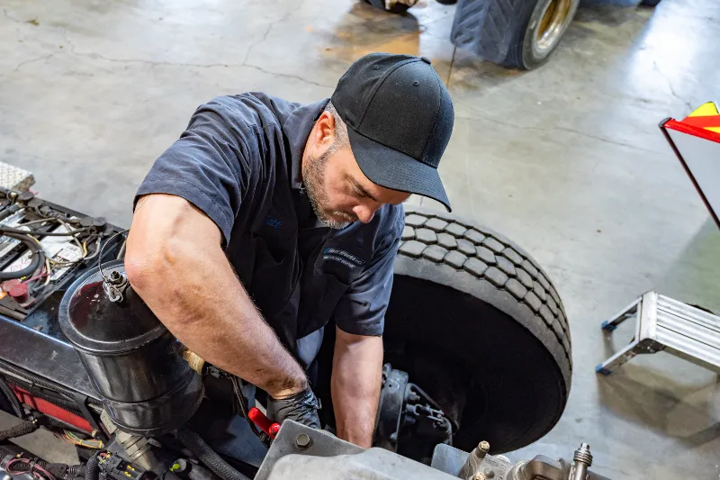 Mechanic performing heavy-duty truck repair near large tire in a service shop.