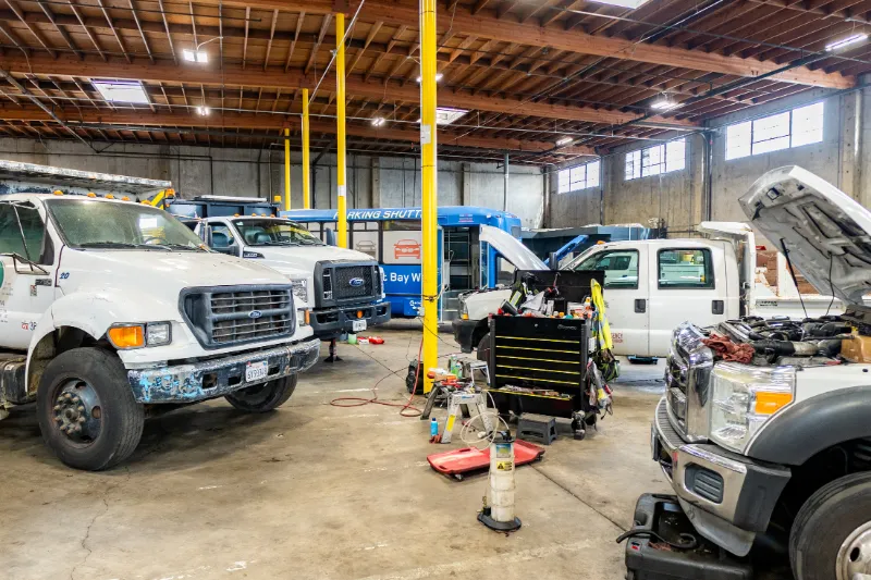 Fleet maintenance service on multiple heavy-duty trucks and a shuttle bus inside a busy repair facility.
