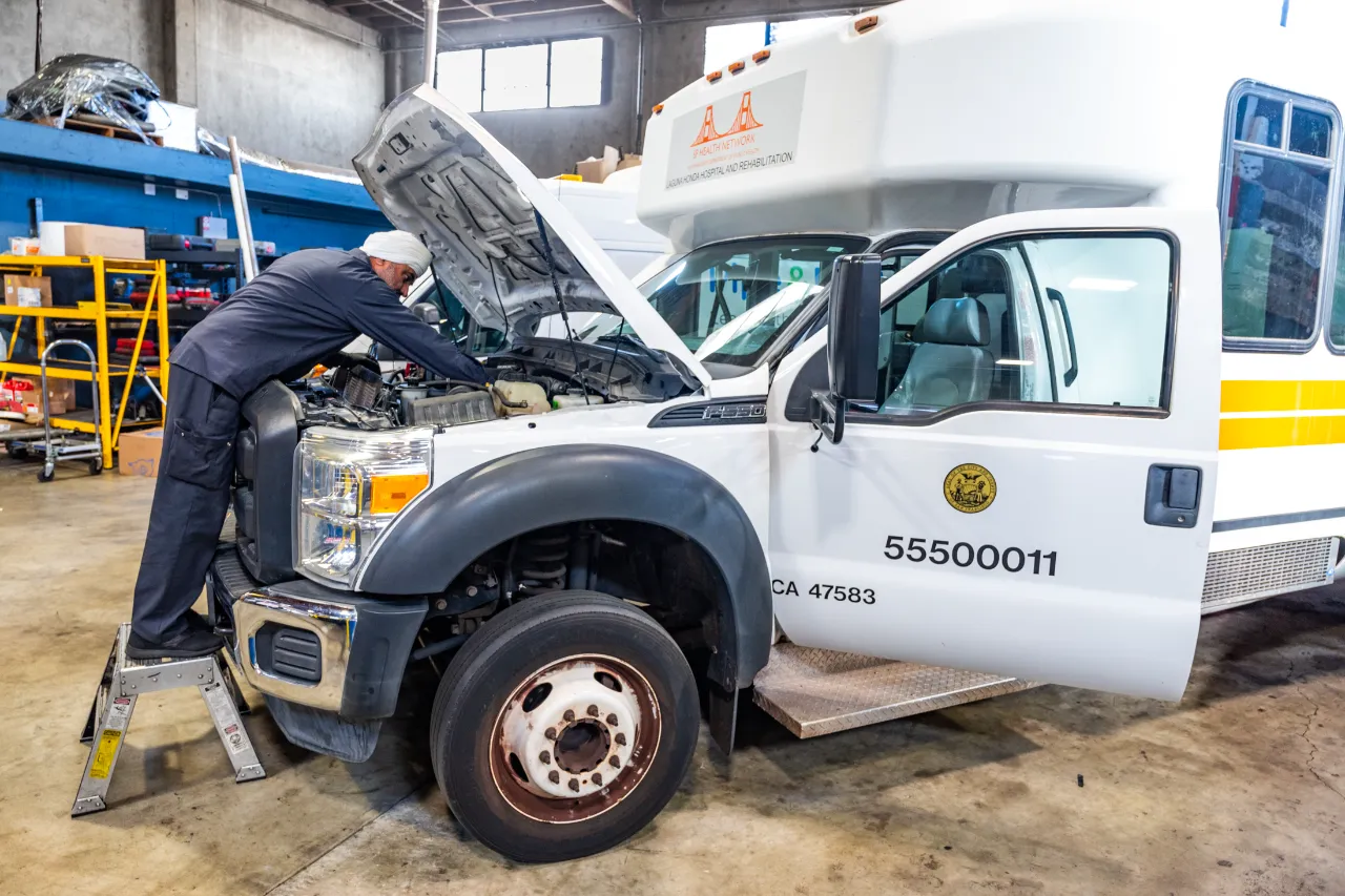 Fleet vehicle repair service on Ford F-550 shuttle bus as tech works under raised hood; unit “55500011” visible.