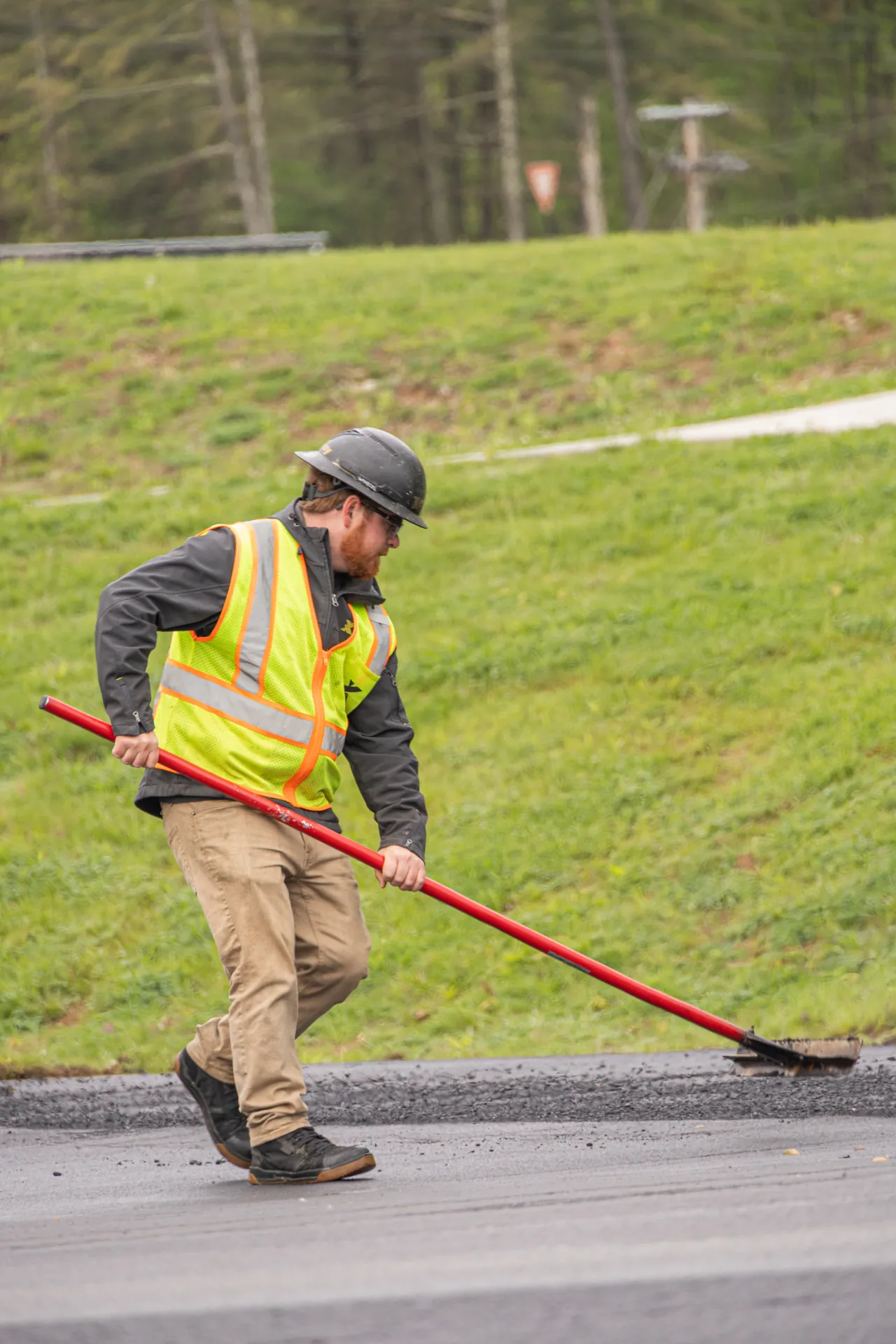 Man with yellow kingsway jacket using a tool to level asphalt