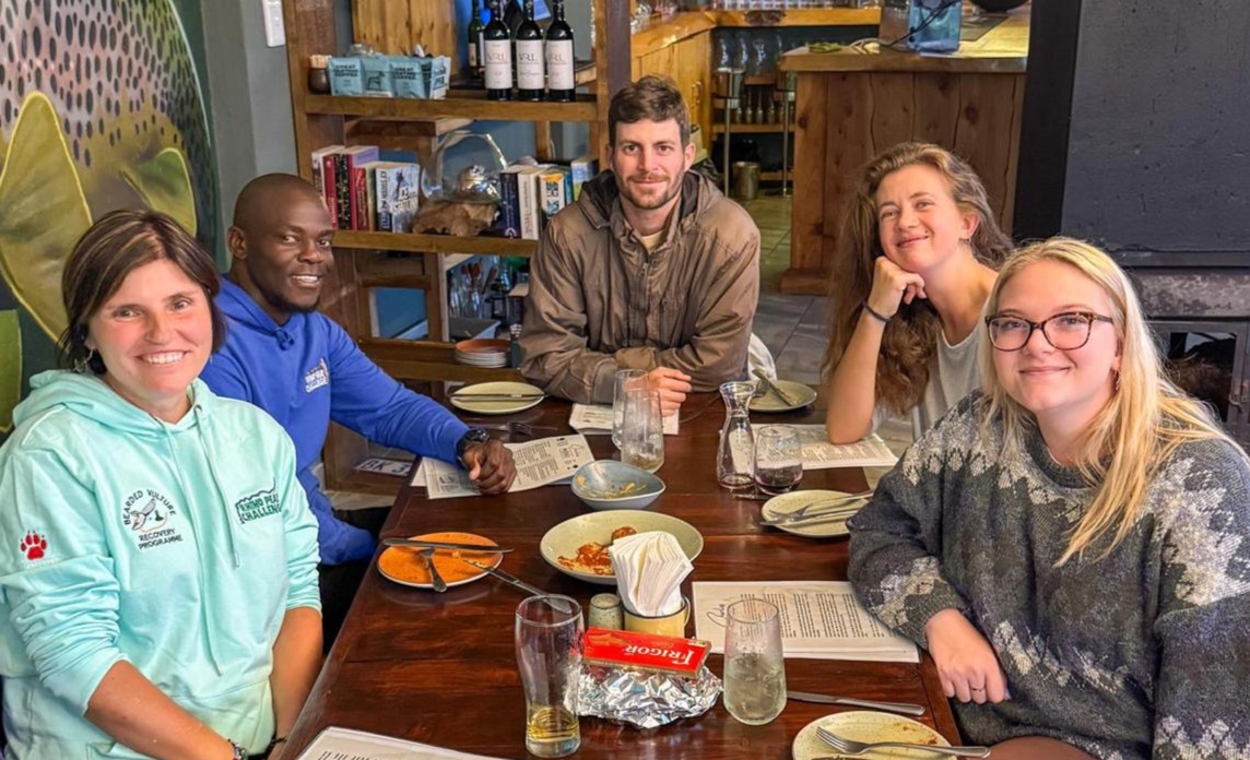 Five people are seated around a table in a cafe, some are part of the Wildlife ACT conservation team while others are volunteers, they smile at the camera