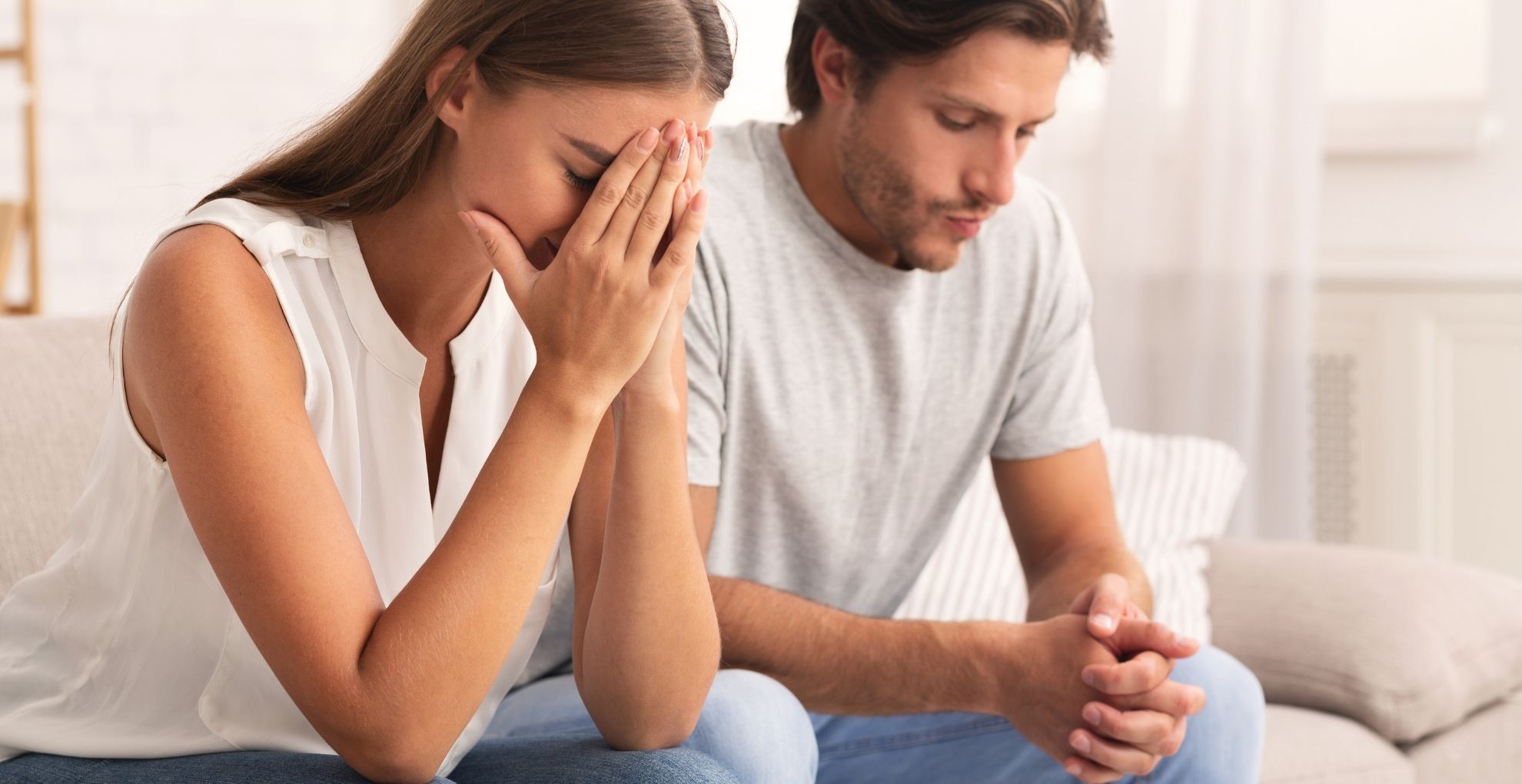 Man en vrouw naast elkaar op de bank met emoties in gezichten waarbij vrouw handen voor het gezicht heeft