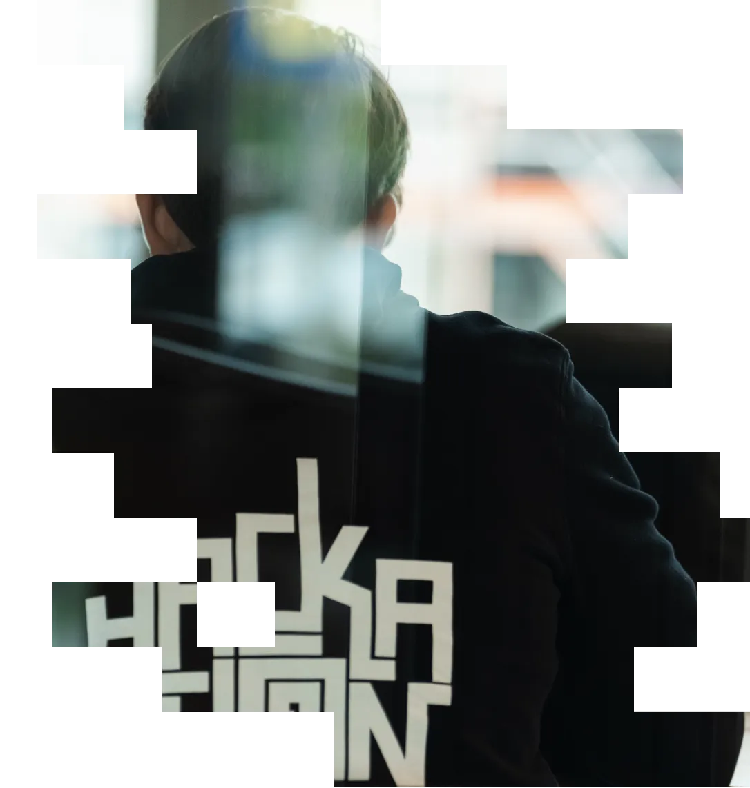 Person seen from behind wearing black hoodie with white text 'Hackathon' near a window.