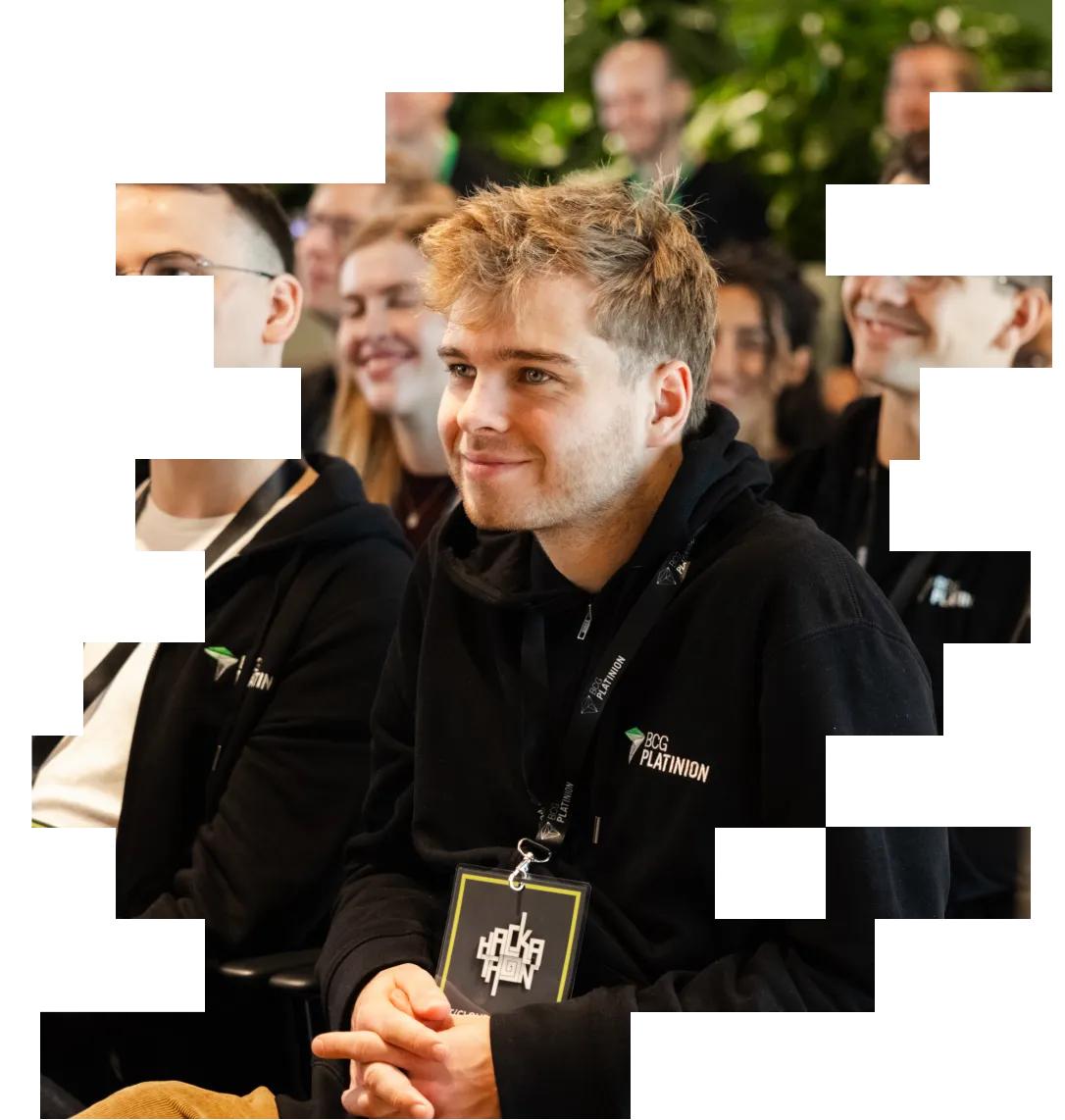 Young man smiling in black BCG Platinion hoodie at the Hackathon event with attentive audience in background.