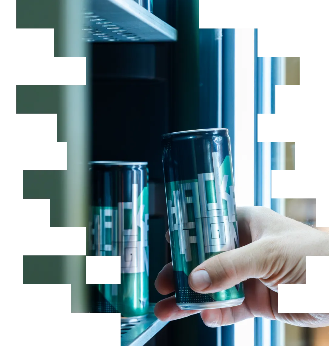 Hand holding a dark aluminum can with geometric design near a shelf with another identical can.