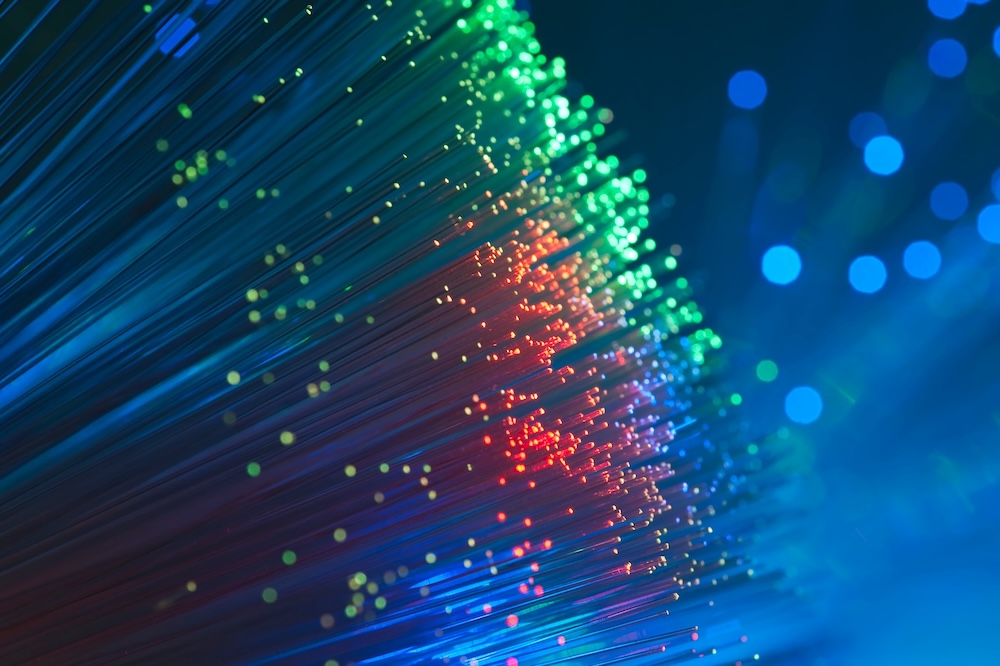 Close-up of fiber optic cables glowing in blue, green, red, and yellow light points on a dark background.