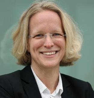 Smiling person with glasses and blonde hair wearing a black blazer and white shirt.