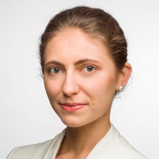 Portrait of a woman with brown hair tied back, wearing pearl earrings and a white top, against a white background.