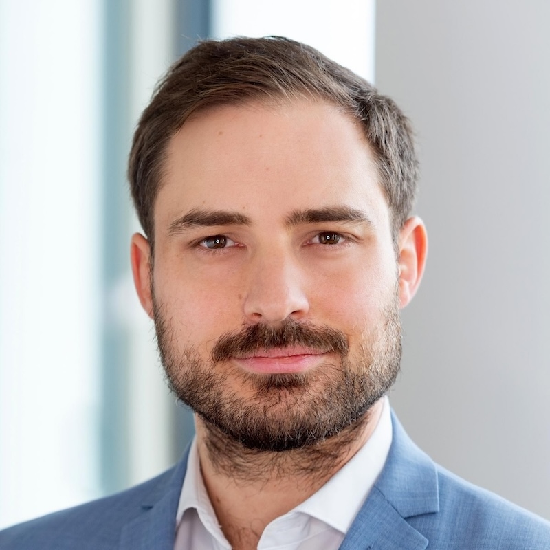 Headshot of a man with short brown hair, beard, and blue suit jacket over a white shirt.