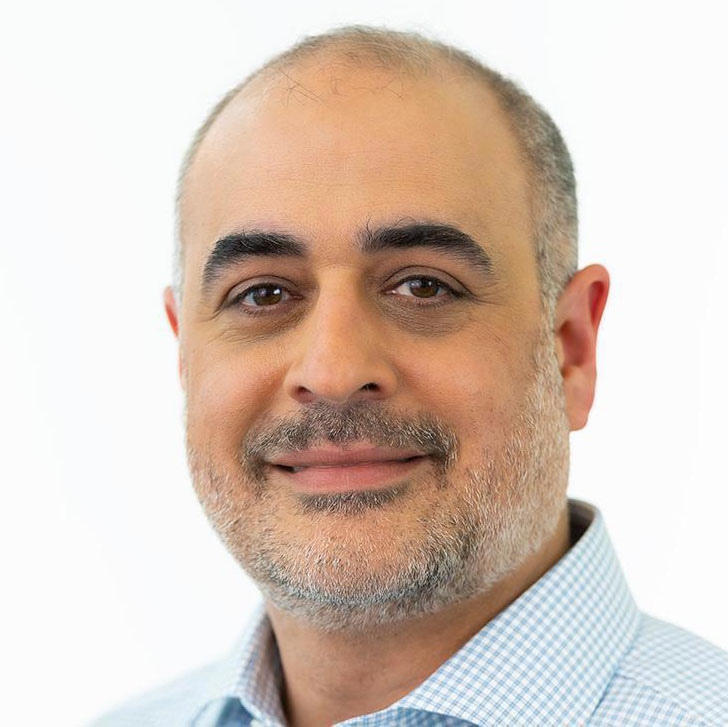 Middle-aged man with short gray hair and beard wearing a light blue checkered shirt, smiling gently.