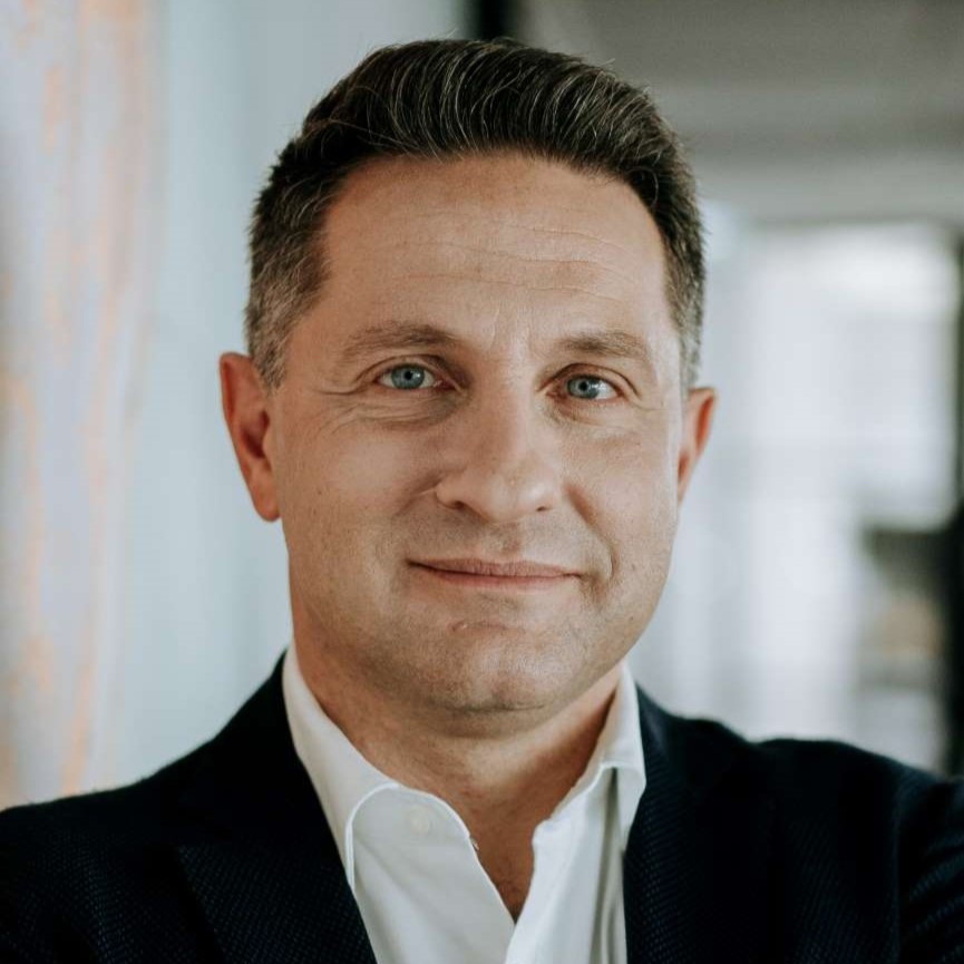 Portrait of a middle-aged man with short dark hair, blue eyes, wearing a white shirt and dark jacket.