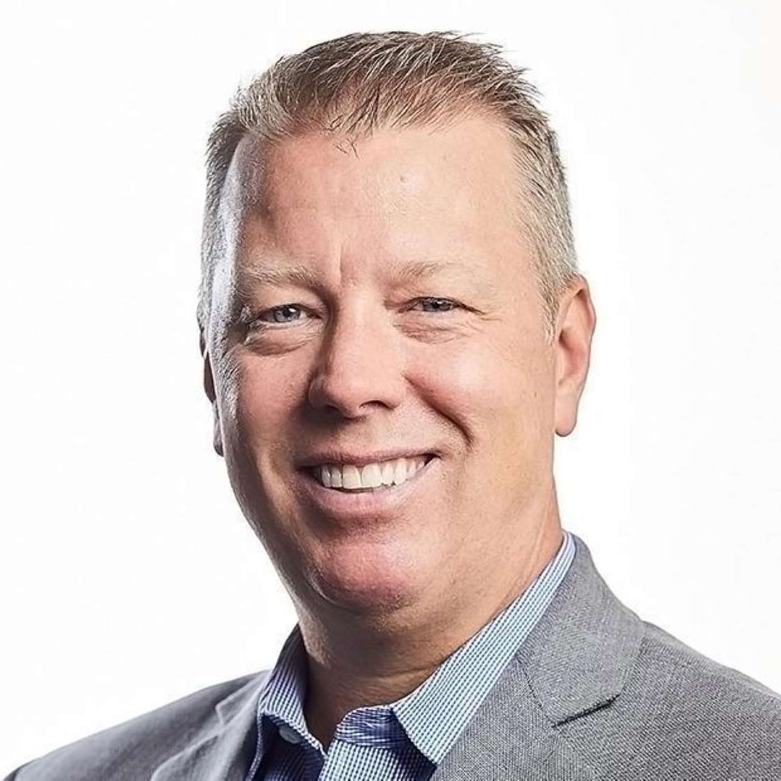Smiling middle-aged man with short light hair wearing a gray suit jacket and blue striped shirt.