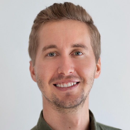 Portrait of a smiling young man with light brown hair and blue eyes wearing a green shirt.