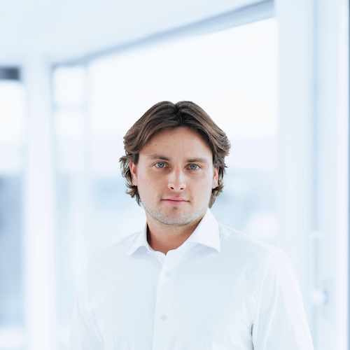 Young man with brown hair and blue eyes wearing a white shirt in bright indoor setting.