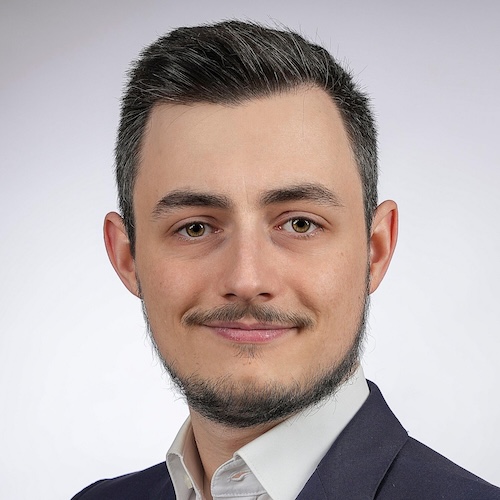 Portrait of a man with short dark hair, beard, and mustache wearing a suit jacket and white shirt.