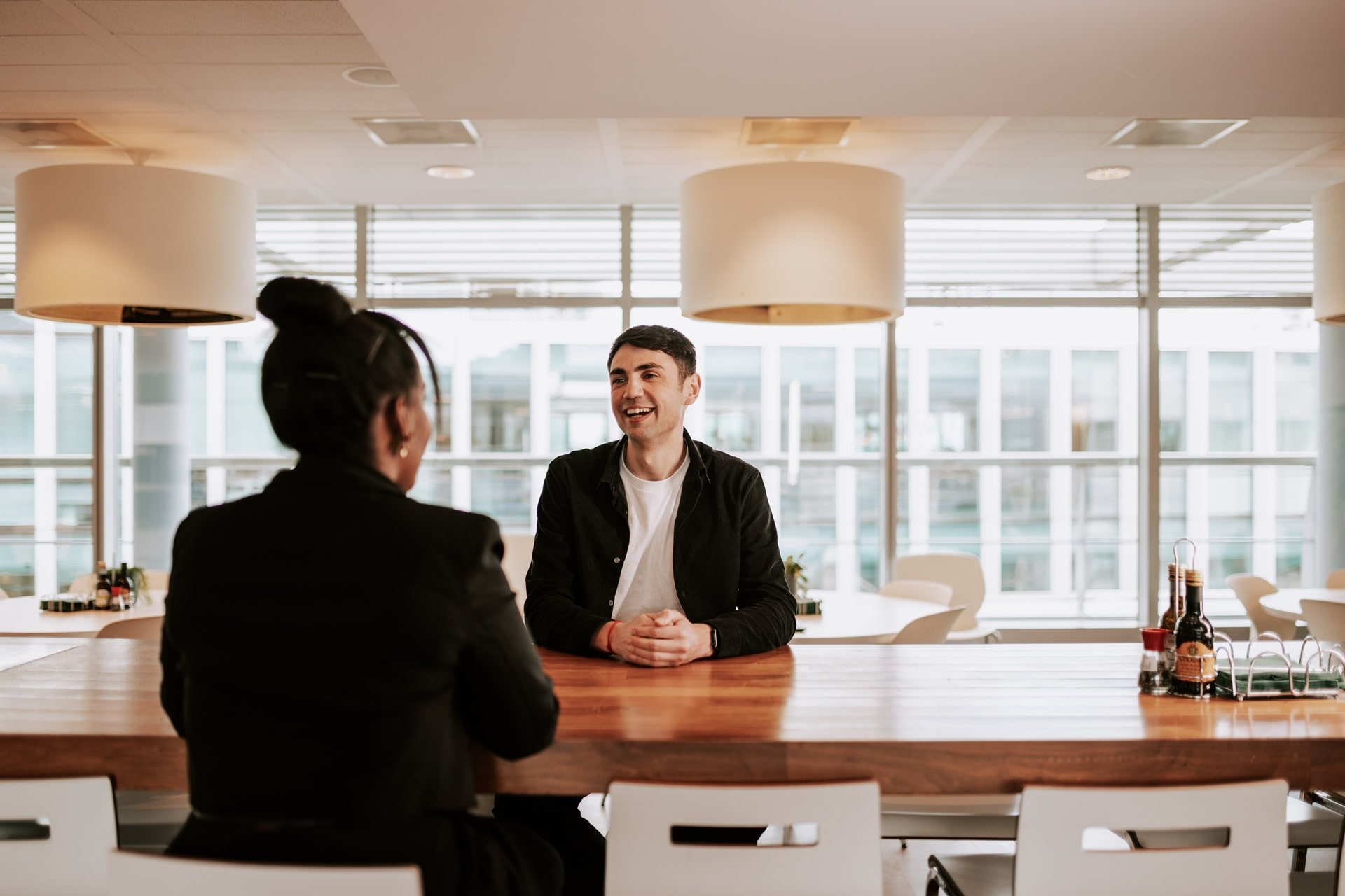 Two people sitting across a table in a bright modern room engaging in conversation.
