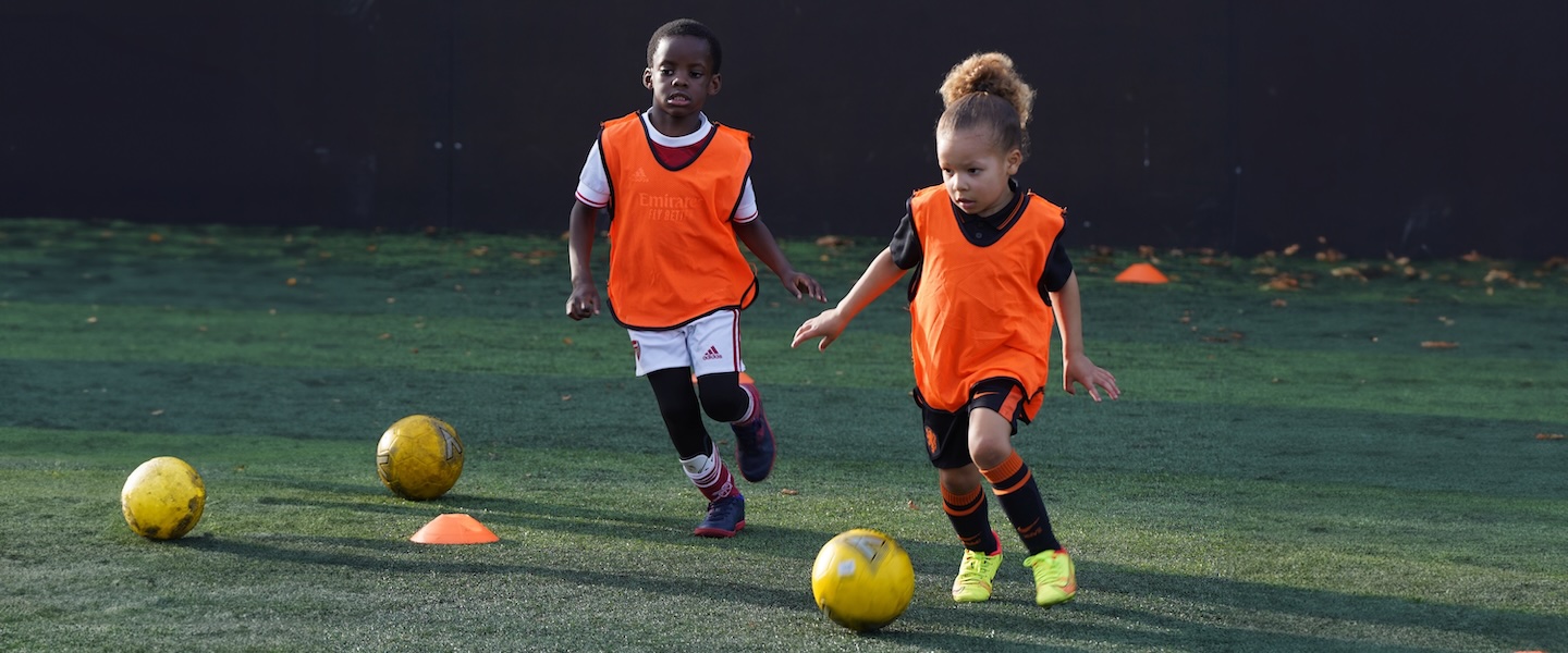 kids playing football with orange bib and yellow ball