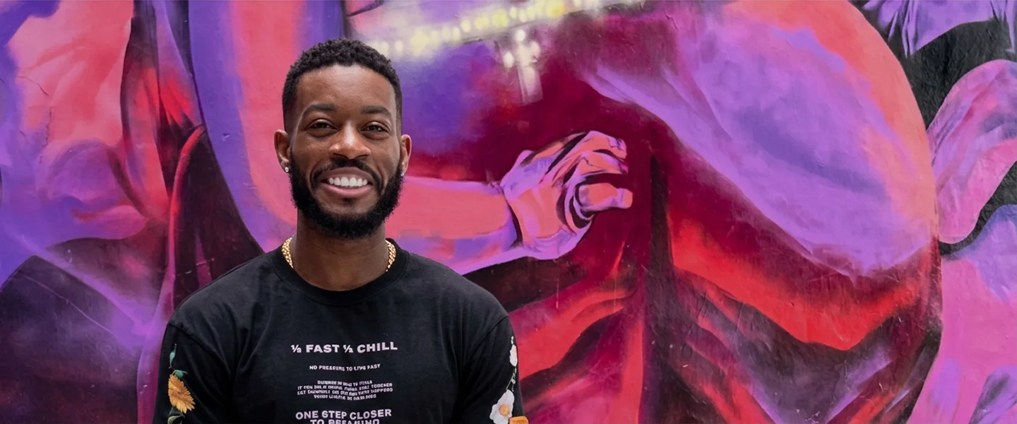 Mojo smiling in front of a colorful mural with abstract designs.