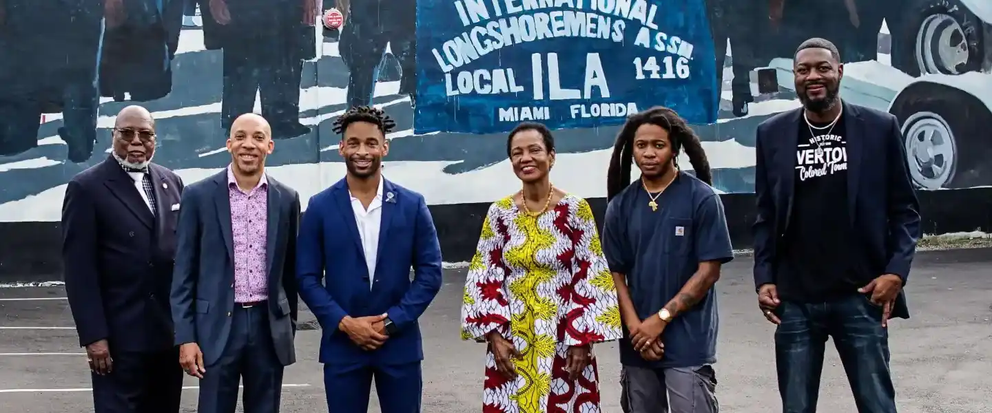Group of people in front of a mural depicting longshoremen.