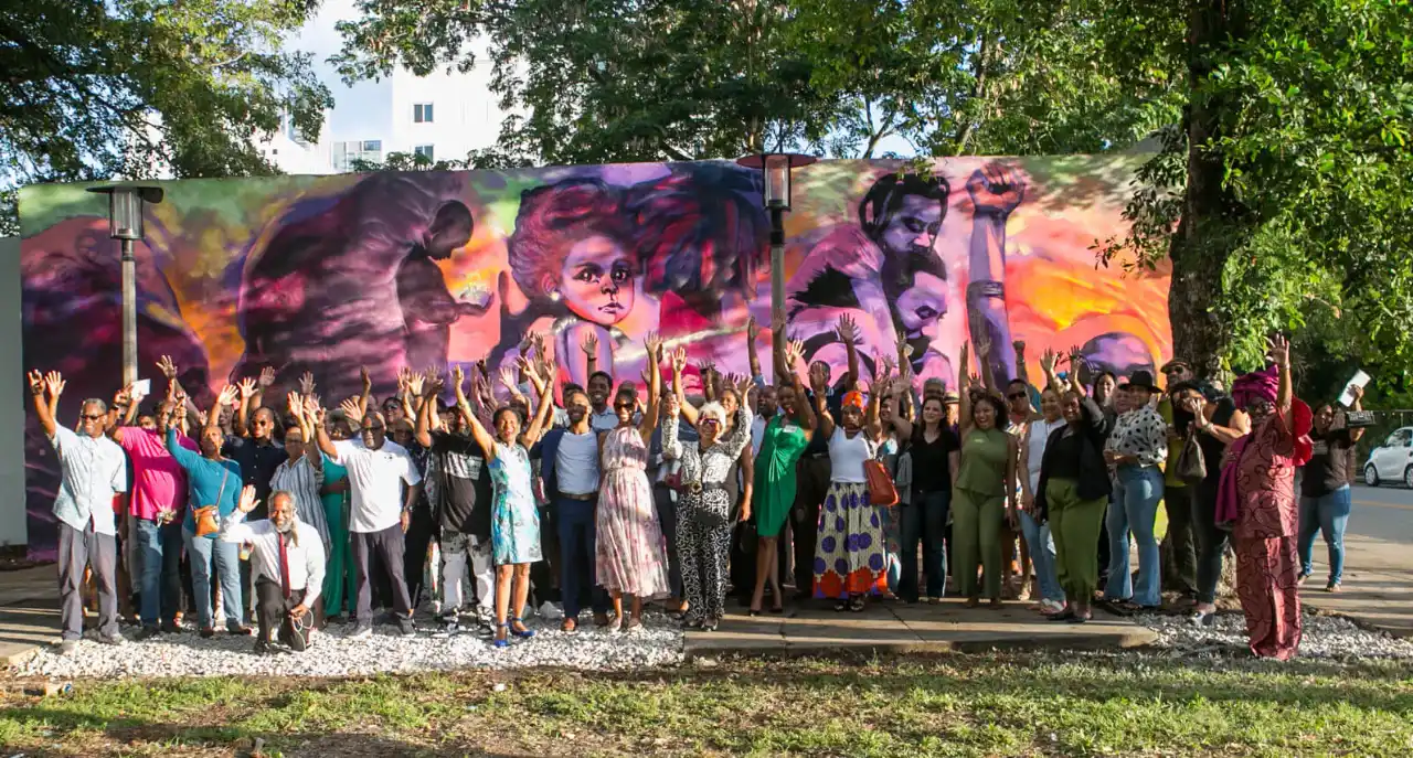 Large group celebrating in front of a colorful mural.