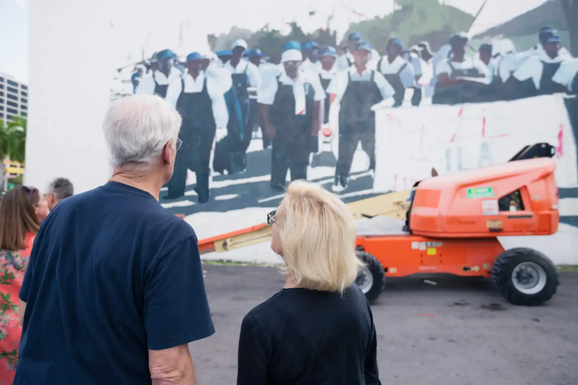 Two people looking at a mural with construction lift in front.