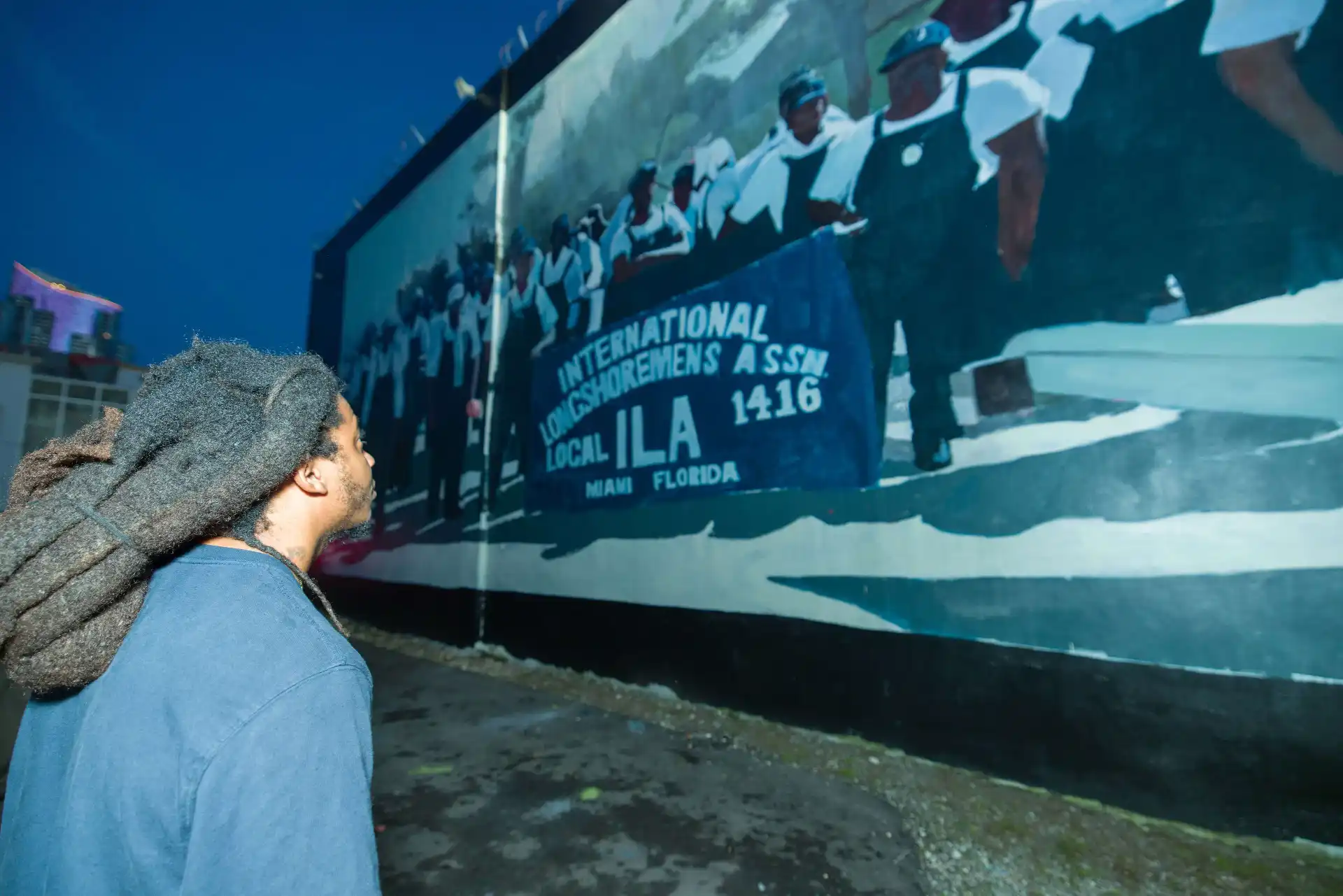 Person viewing a mural of longshoremen at dusk.