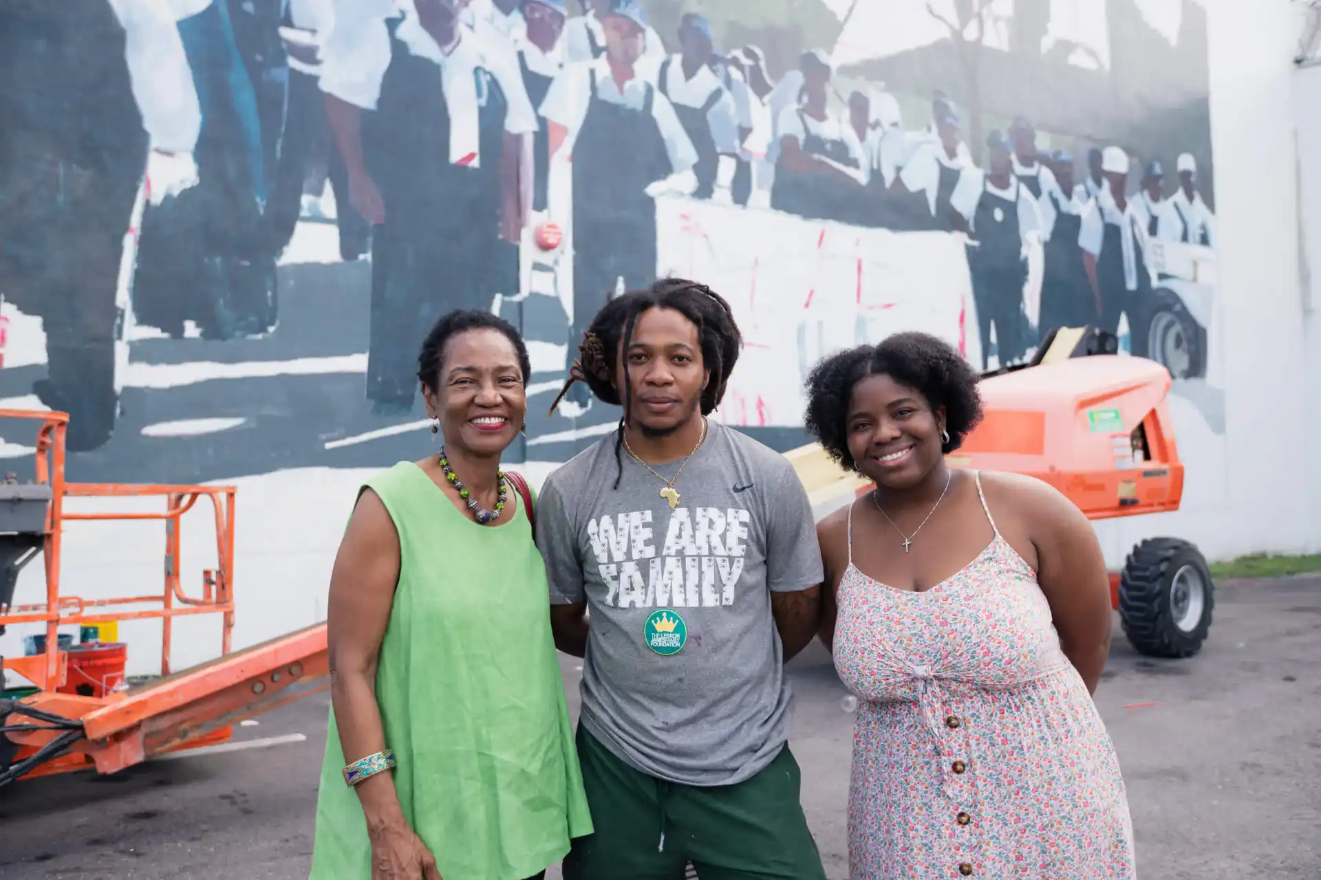 Three people smiling in front of a historical mural.