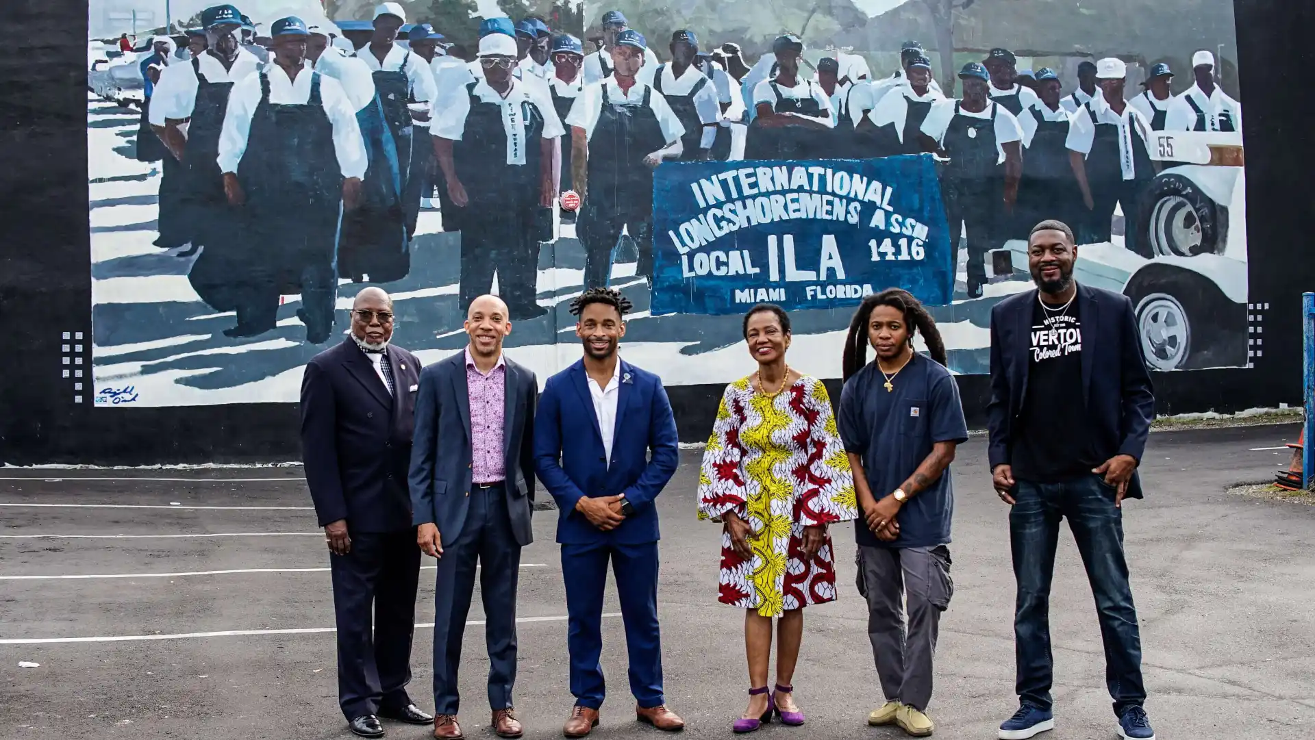 Group of people in front of a mural depicting longshoremen.