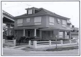 Vintage black and white photo of a two-story house with a porch.