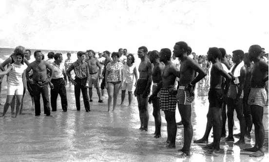 People standing in a line on a beach, facing inland.