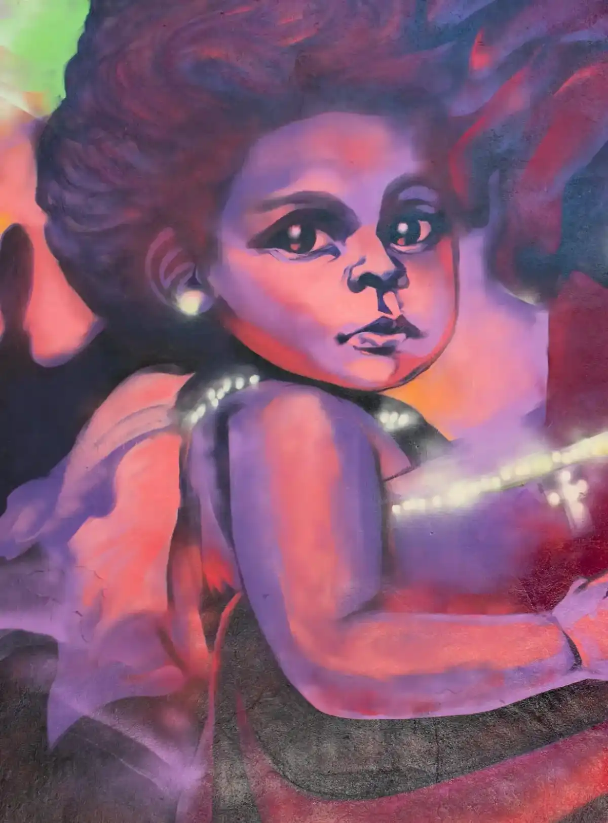 Artist in a white hat and shirt painting a vibrant mural of a child with large eyes and colorful abstract shapes.