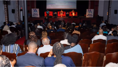 Audience seated in a theater watching a panel discussion on stage with a red carpet and banners reading MCAD.