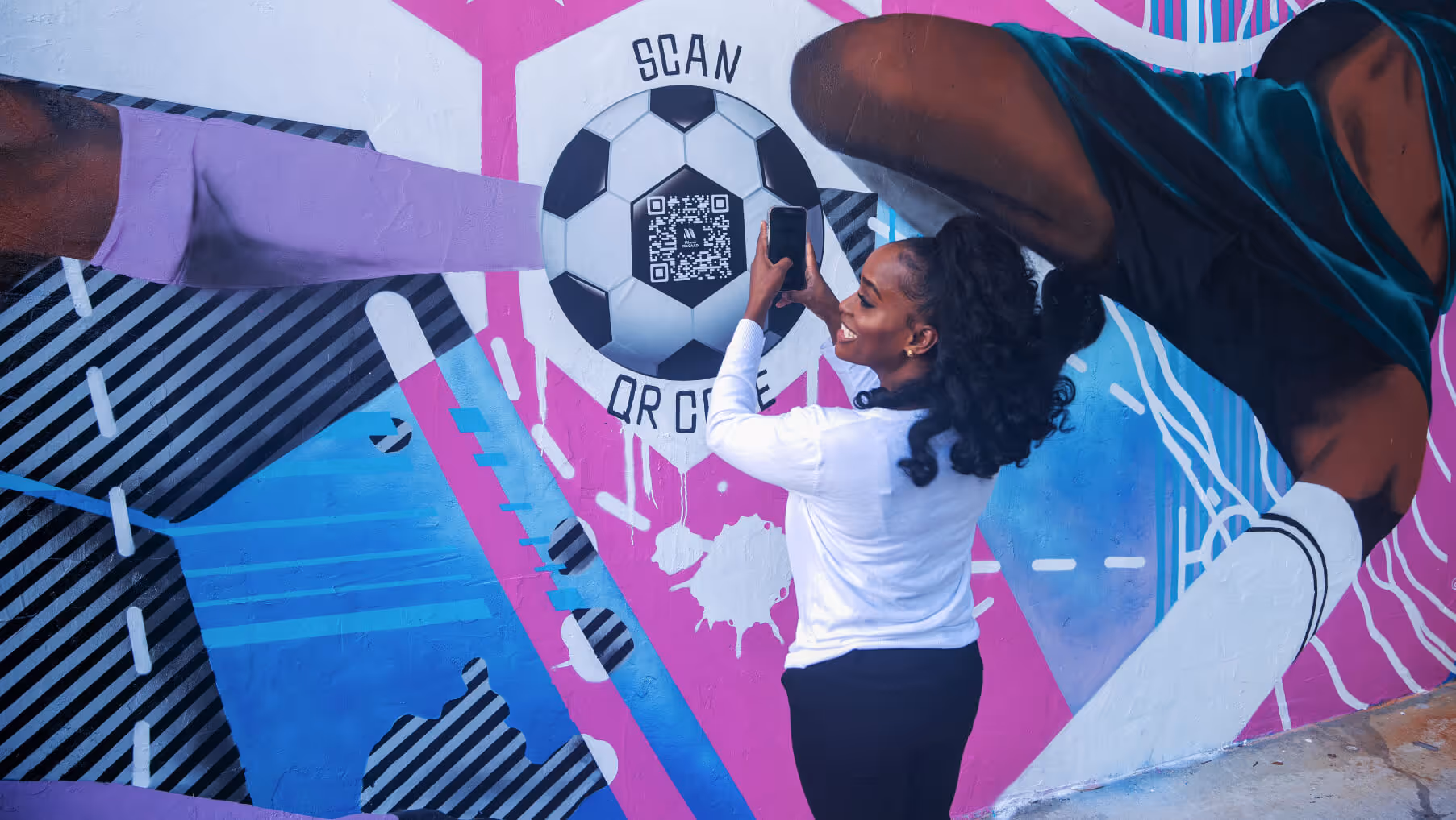 Woman using her phone to scan a QR code embedded in a soccer ball in colorful street art.