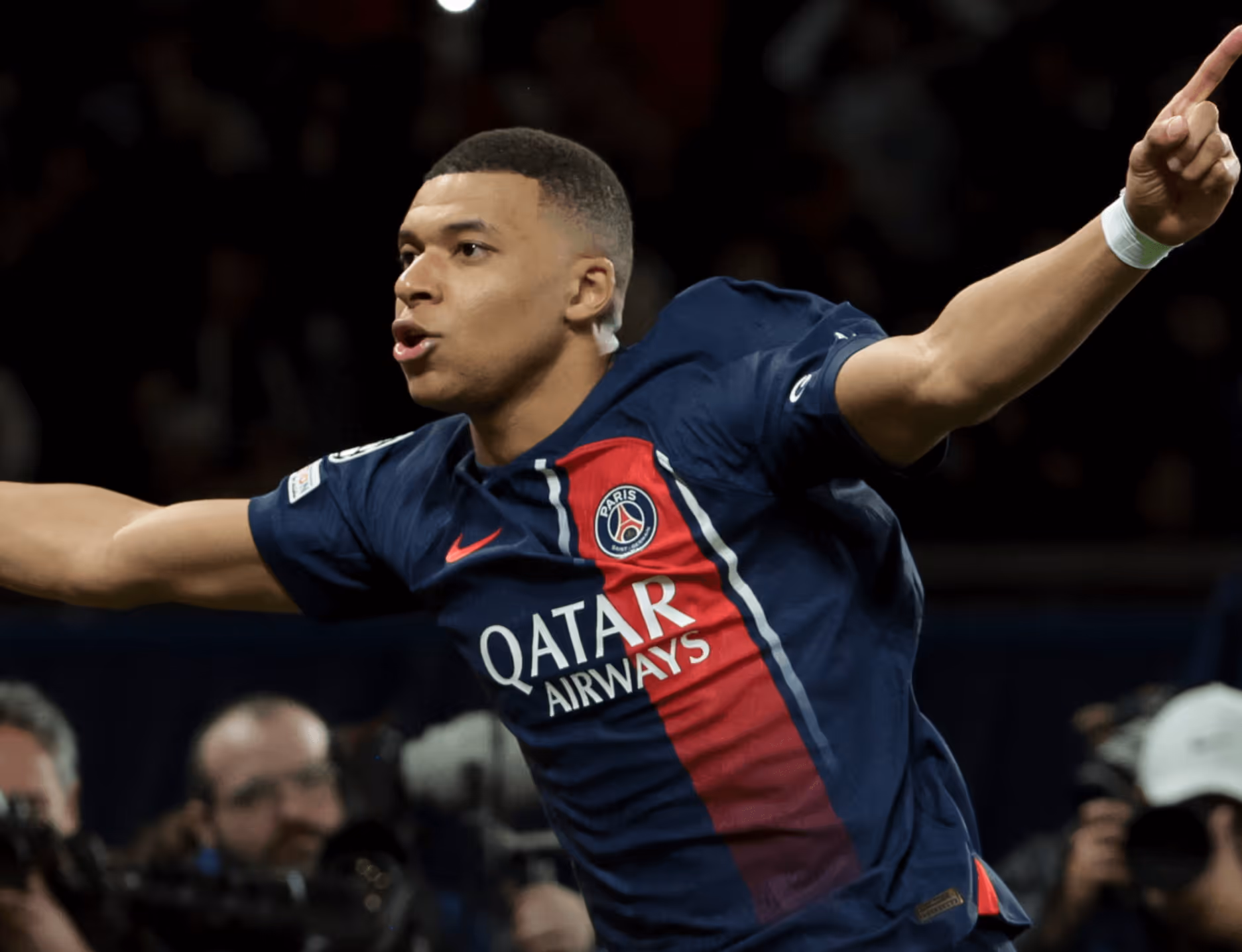 Soccer player in Paris Saint-Germain jersey celebrating with arms outstretched during a match.