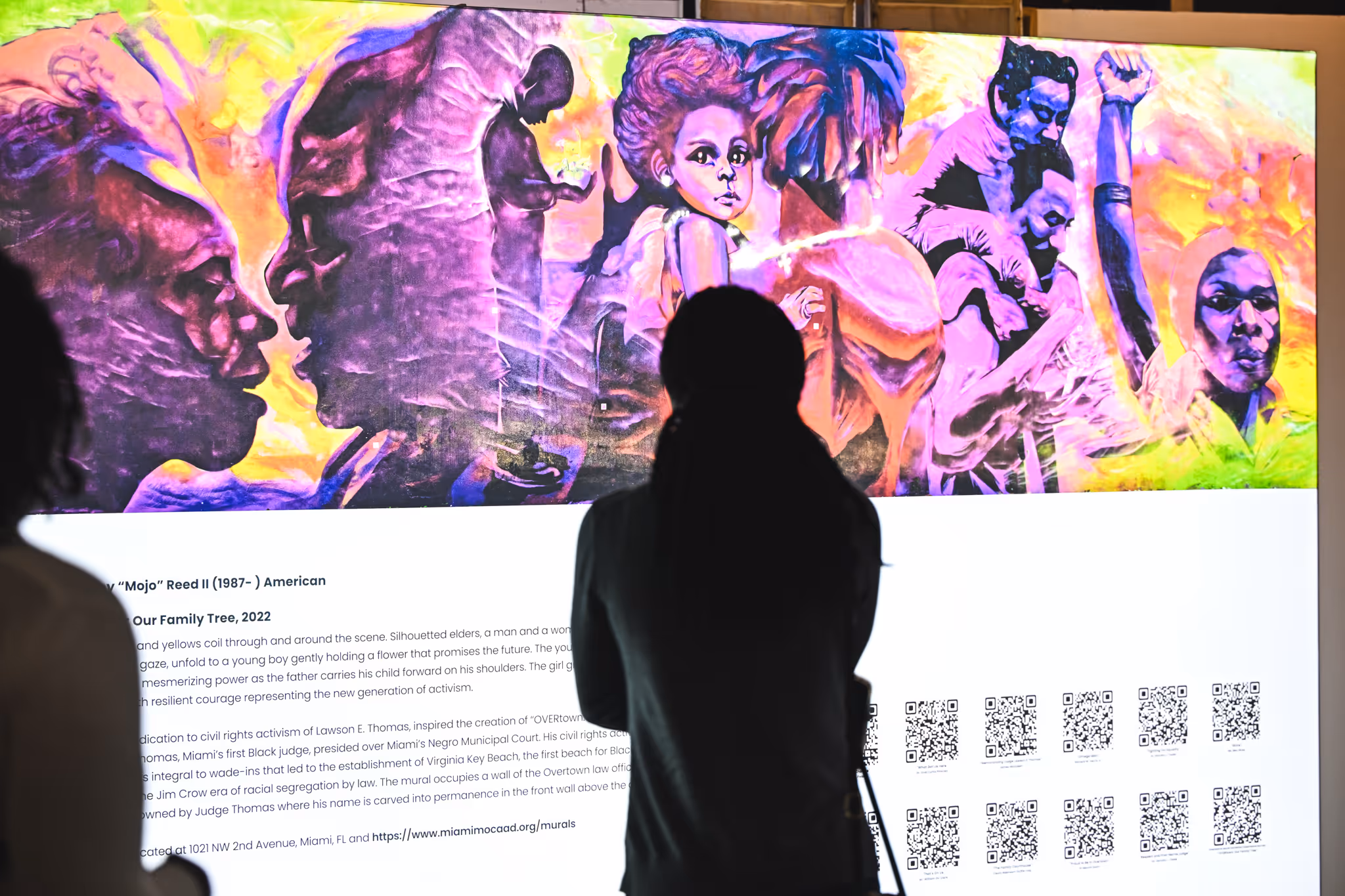 Silhouetted person viewing a vibrant mural depicting diverse figures symbolizing family, activism, and hope.