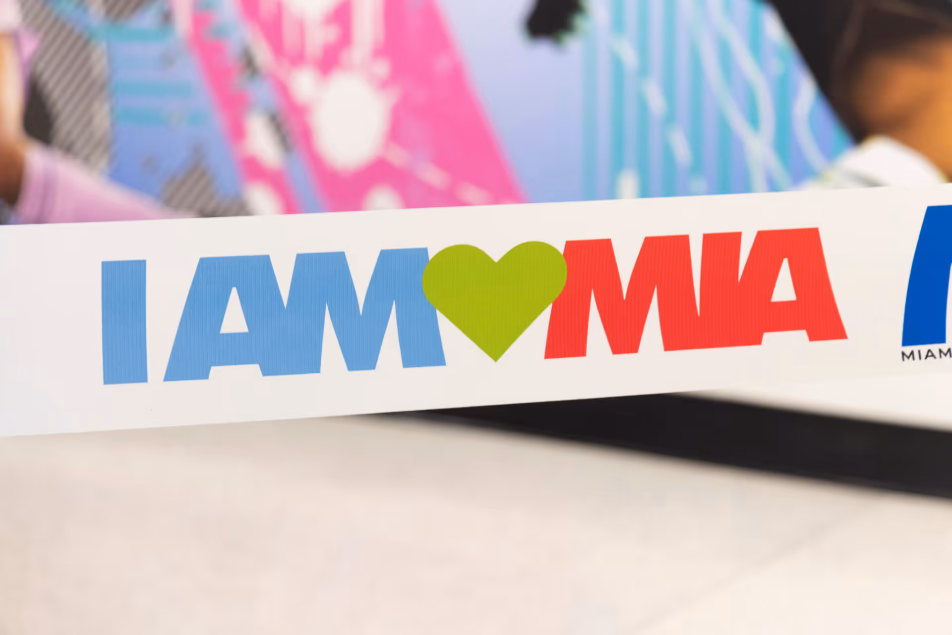Sign with text 'I AM' in blue, a green heart, and 'MIA' in red.