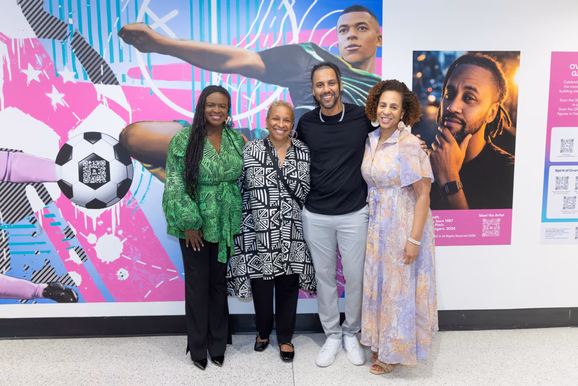 Four people smiling and standing in front of a colorful mural with a soccer theme.