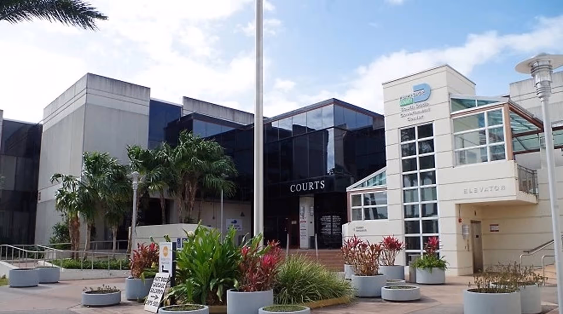 Modern courthouse building with palm trees and landscaping in front under blue sky.
