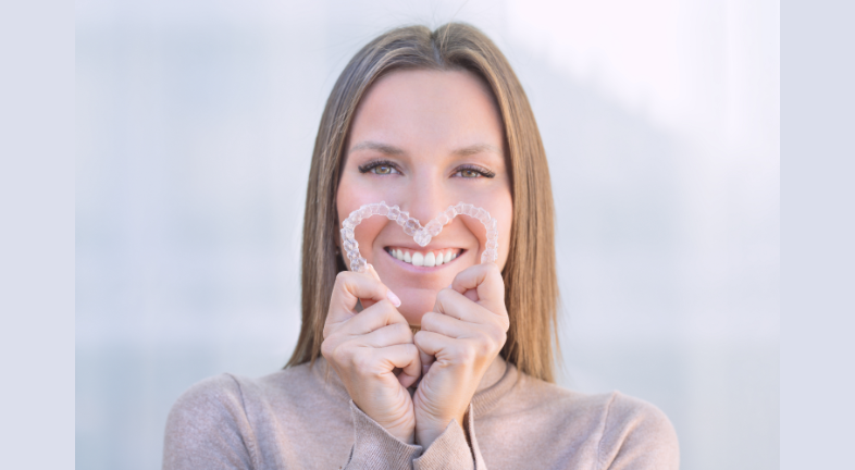 A girl holding and making a heart with clear aligners 