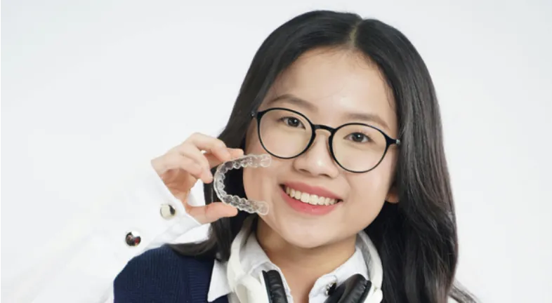 A teenage girl holding clear aligners 