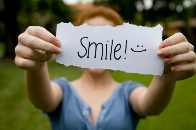 A girl holding a paper with “smile” written on it, depicting smile anxiety