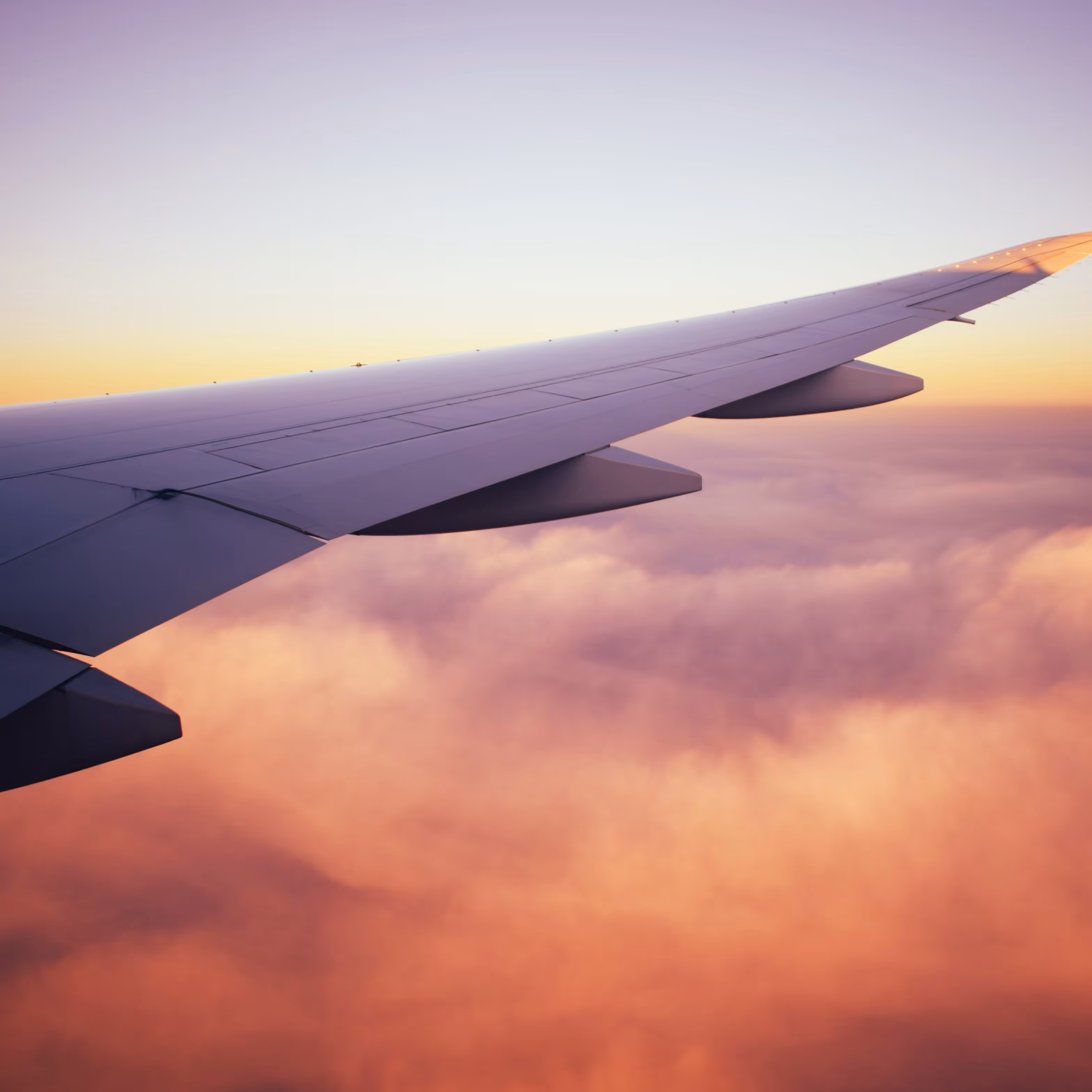 View into sunset clouds from the airplane illuminator where wing is part of the marvelous view.