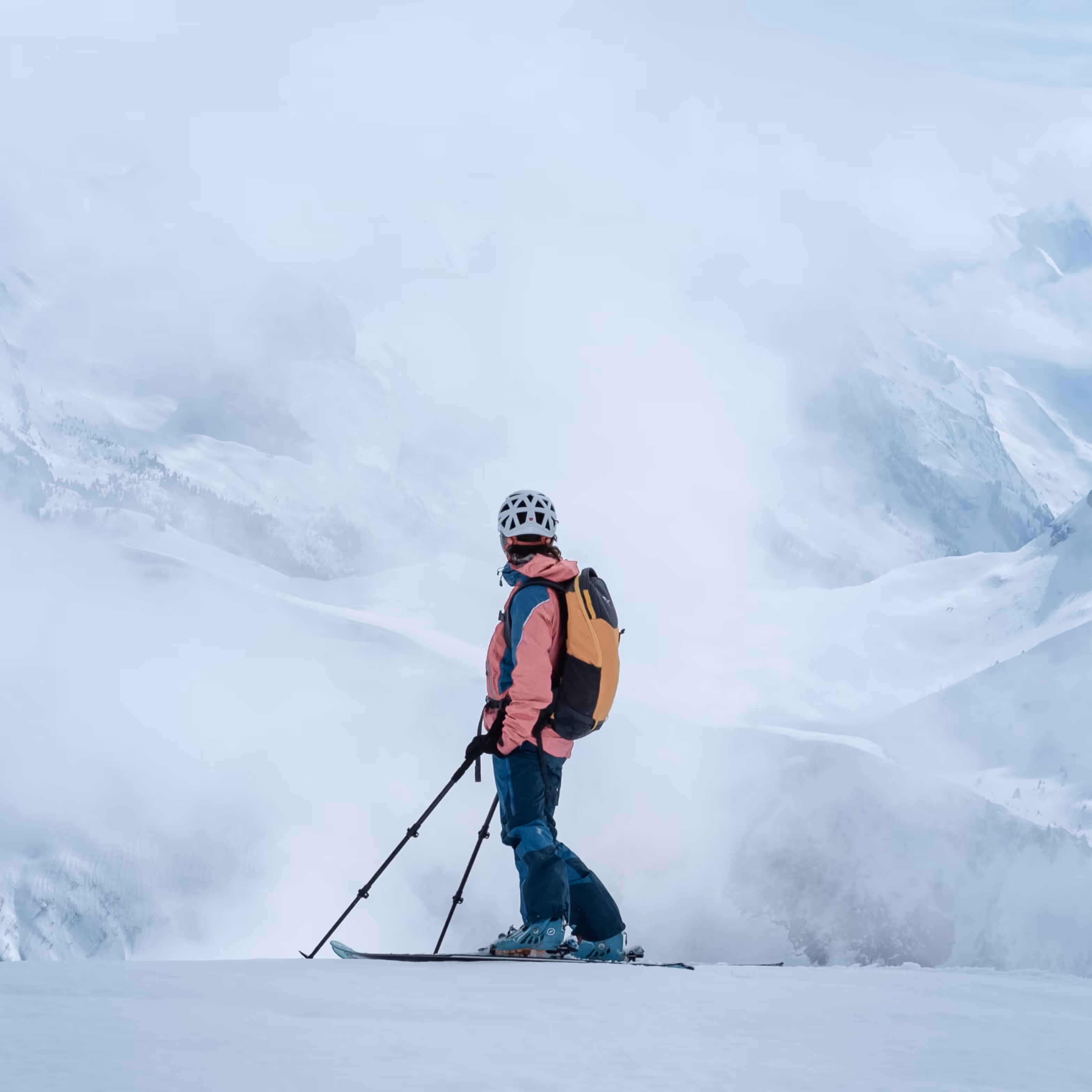 Skiing view person observed from the back on top of the snow mountain observing into distance of massive snow mountains.