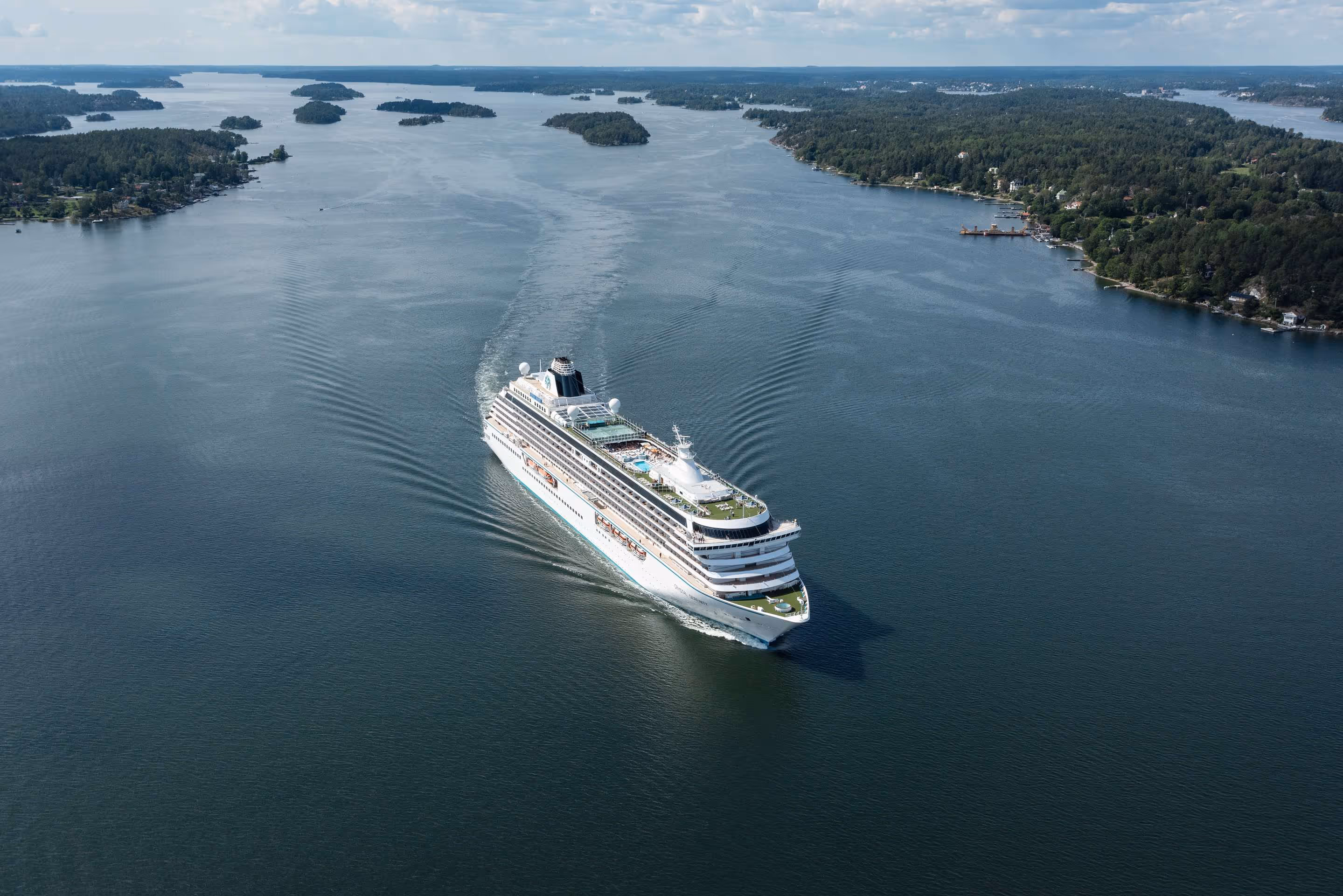 Cruise ship from top in sea next to green lands leaving a bay during a sunny day.