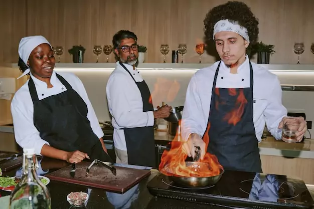 Un jeune cuisinier prépare un steak flambé marbré tandis que son collègue le regarde avec enthousiasme