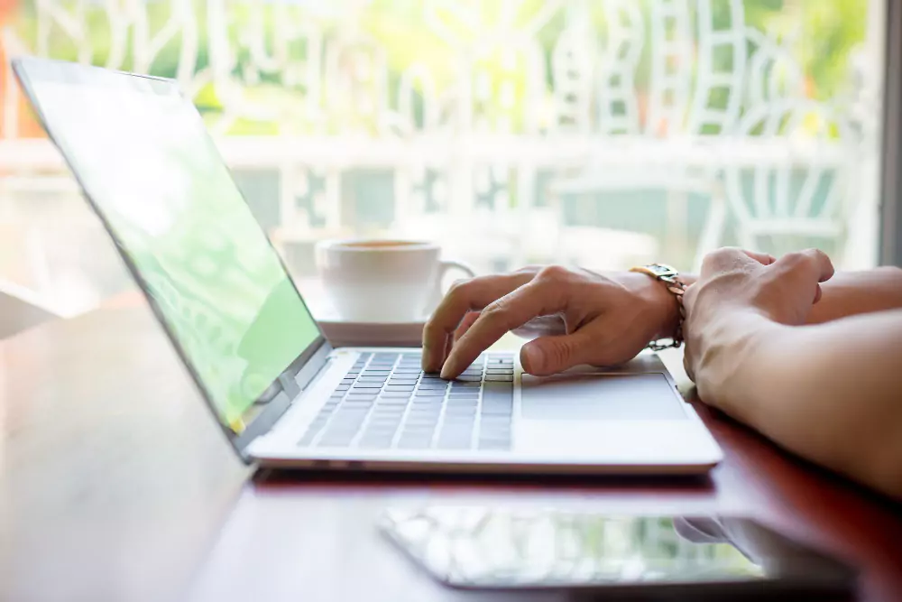 Main d'homme tapant sur un ordinateur portable dans un café